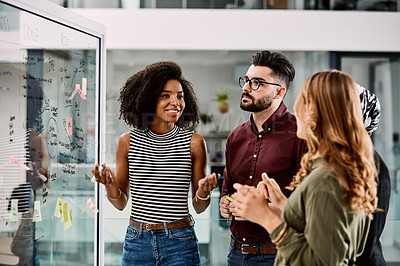 Buy stock photo Shot of a group of young businesspeople planning and writing notes on a glass wall in an office at work