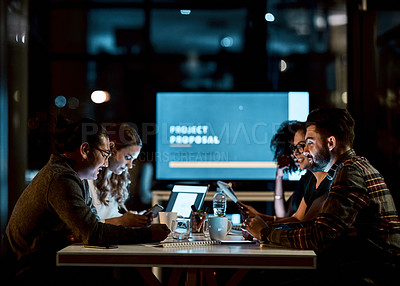 Buy stock photo Shot of a group of young businesspeople using smart devices during a late night meeting at work