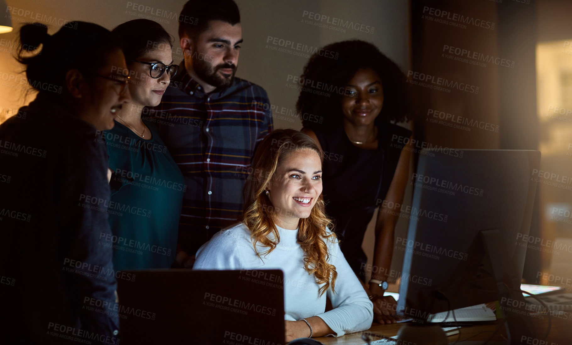 Buy stock photo Shot of a group of young businesspeople using a computer during a late night at work