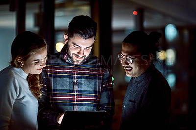Buy stock photo Shot of a group of young businesspeople using a digital tablet during a late night at work