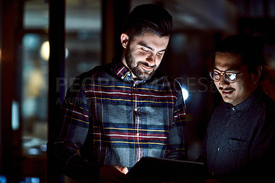 Buy stock photo Shot of two young businessmen using a digital tablet during a late night at work