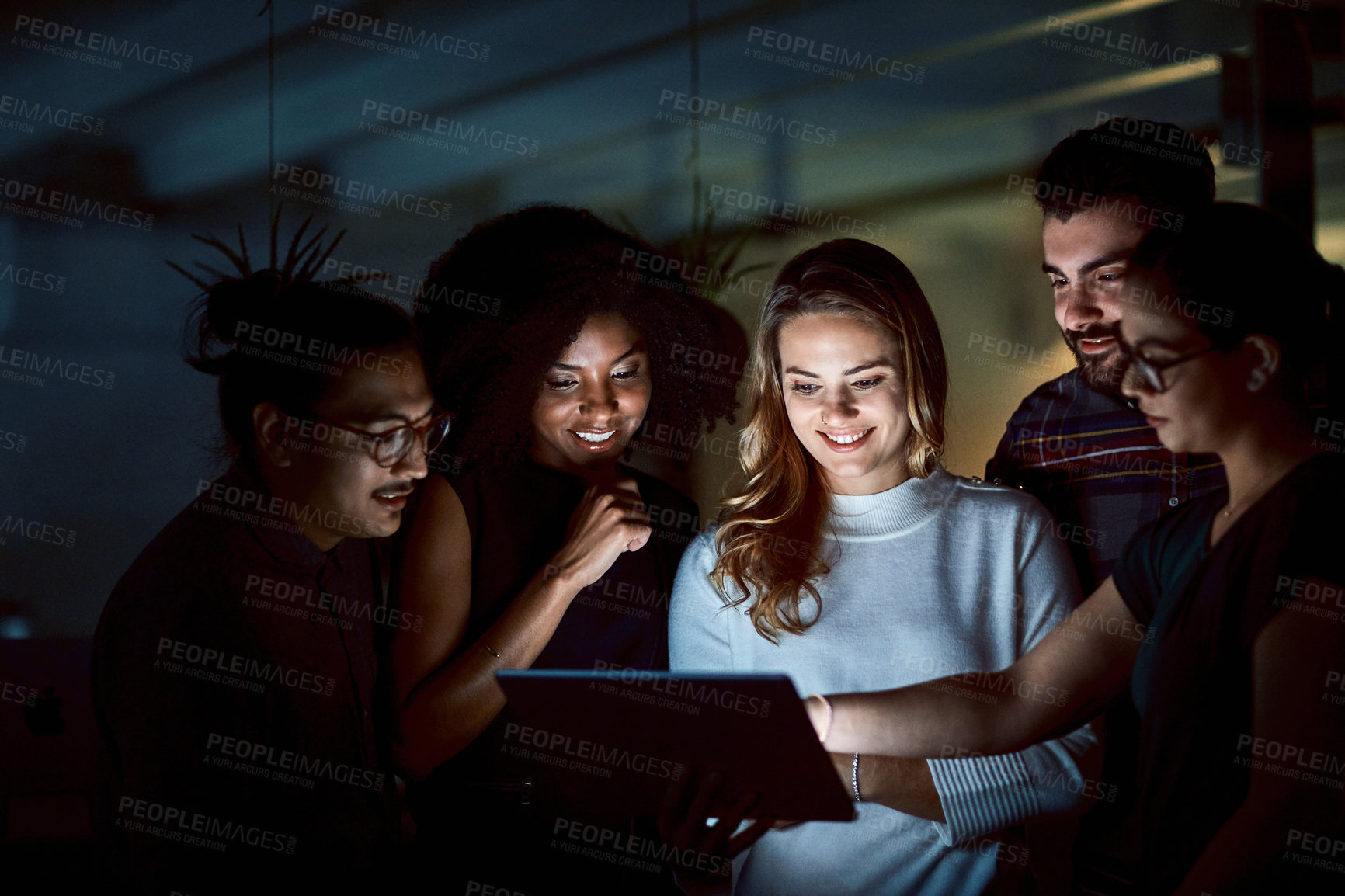 Buy stock photo Shot of a group of young businesspeople using a digital tablet during a late night at work
