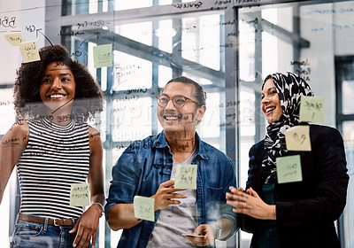 Buy stock photo Shot of a group of young businesspeople planning and writing notes on a glass wall in an office at work