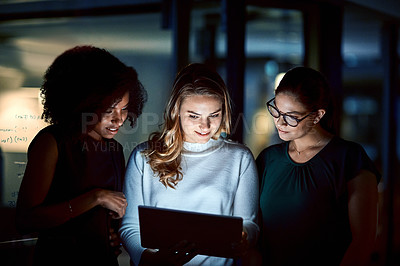 Buy stock photo Shot of a group of young businesswomen using a digital tablet during a late night at work