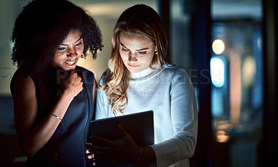 Buy stock photo Shot of two young businesswomen using a digital tablet during a late night at work