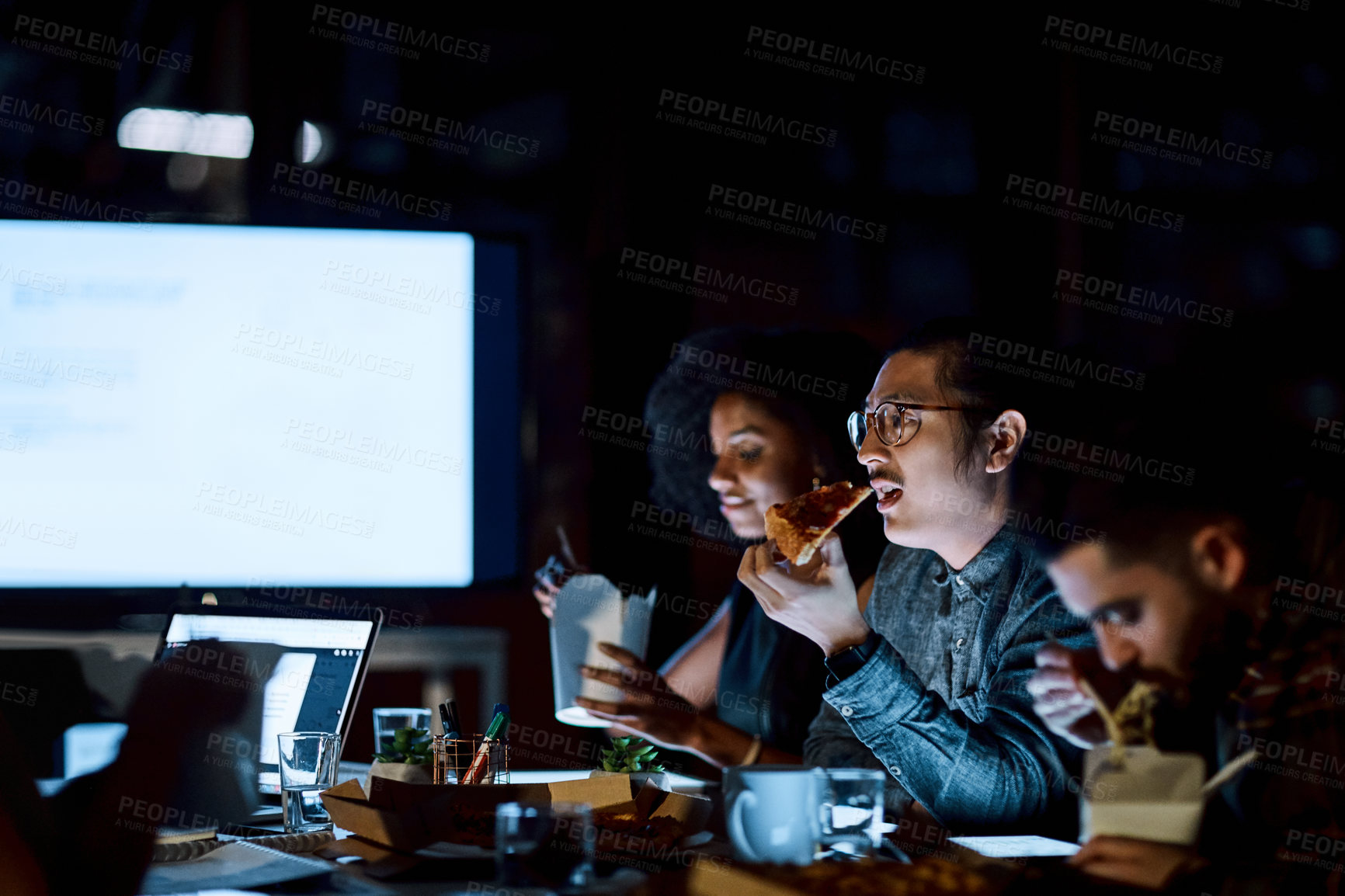 Buy stock photo Shot of a group of young businesspeople having takeout during a late night meeting at work
