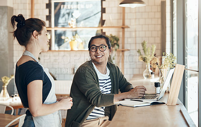 Buy stock photo Shot of a friendly young waitress serving coffee to a handsome young man in a coffee shop during the day
