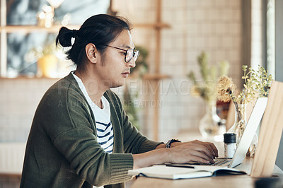 Buy stock photo Shot of a handsome young man sitting and working on his laptop in a coffee shop during the day
