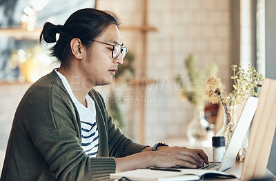 Buy stock photo Shot of a handsome young man sitting and working on his laptop in a coffee shop during the day