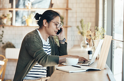 Buy stock photo Shot of a handsome young man working on his laptop and talking on his cellphone in a coffee shop