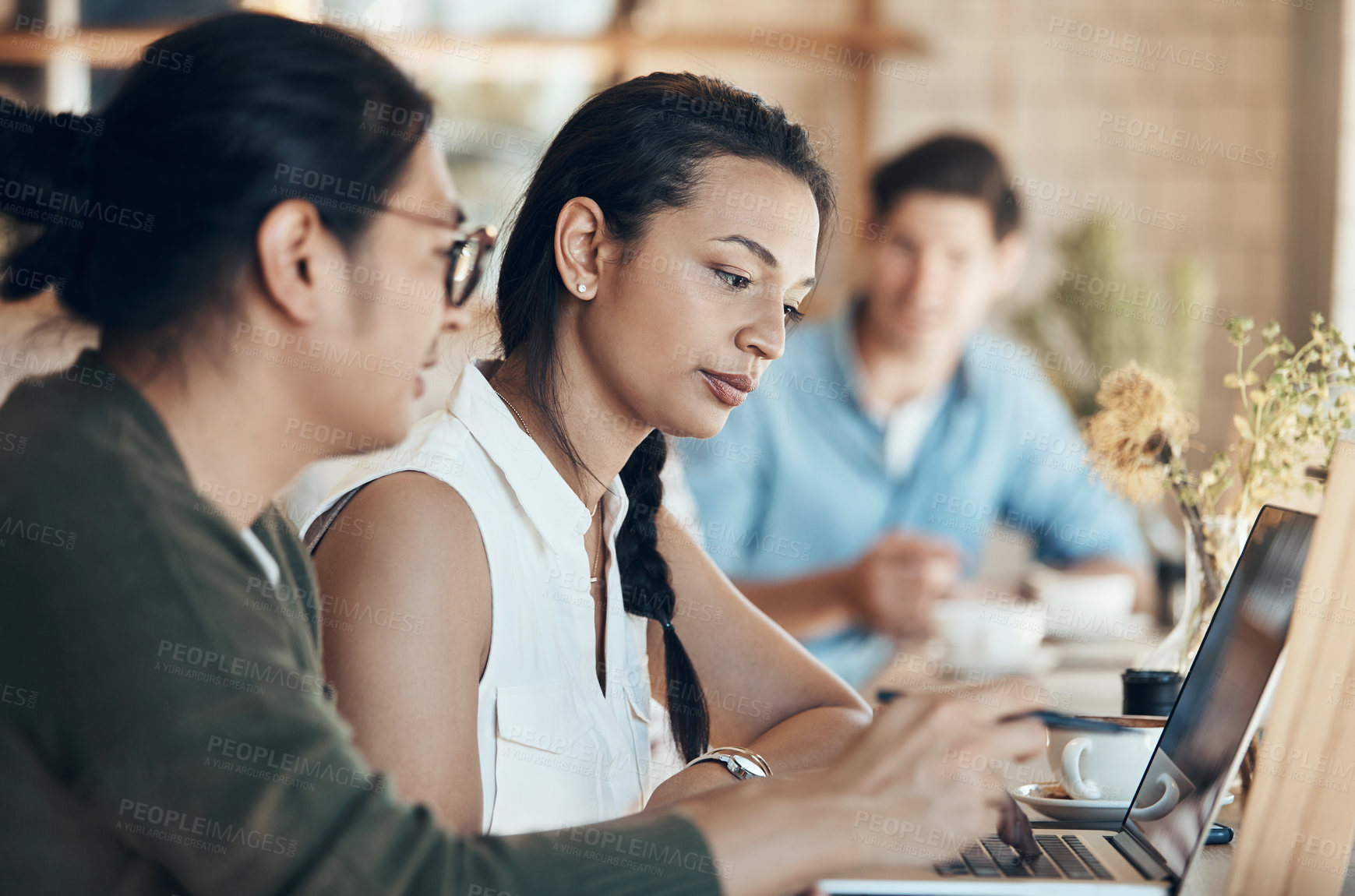 Buy stock photo Shot of young business partners sitting and working with each other in a coffee shop during the day