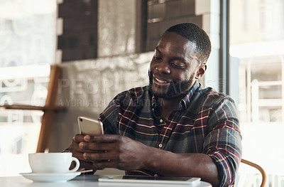 Buy stock photo Shot of a handsome young man sitting and using his cellphone in a coffee shop during the day