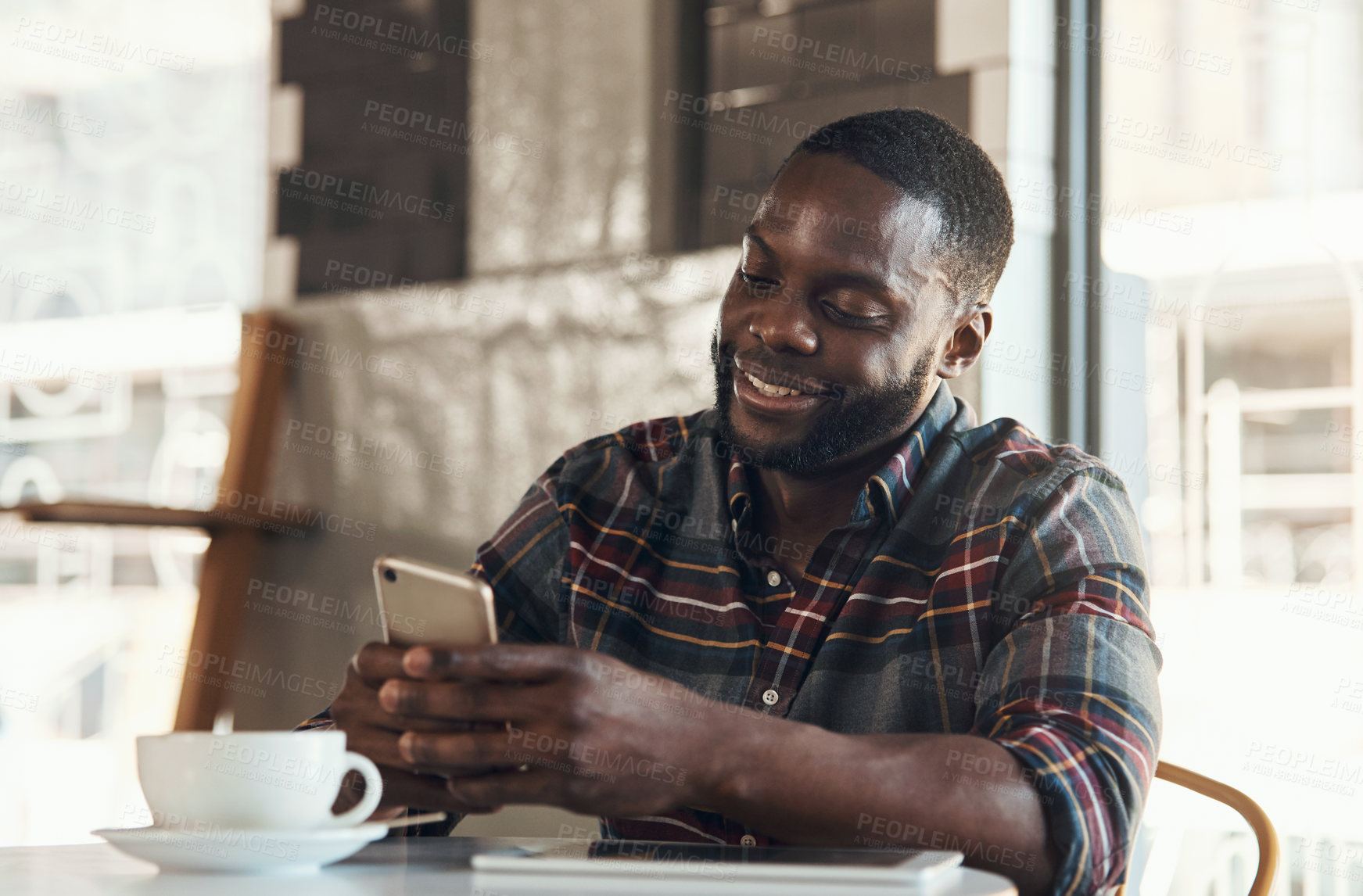 Buy stock photo Shot of a handsome young man sitting and using his cellphone in a coffee shop during the day