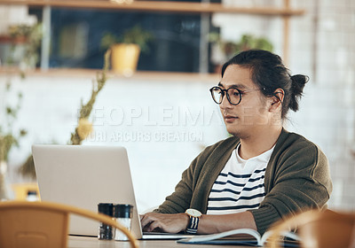 Buy stock photo Shot of a handsome young man sitting and working on his laptop in a coffee shop during the day