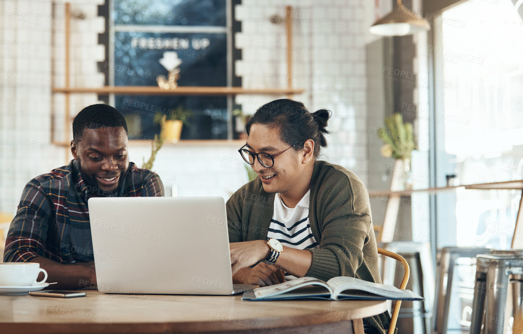Buy stock photo Shot of handsome young businessmen sitting and working on a laptop in a coffee shop during the day