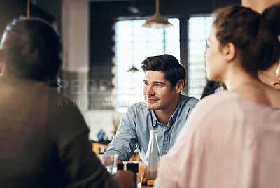 Buy stock photo Shot of a handsome young man sitting and smiling with his friends in a coffee shop during the day
