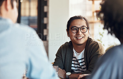 Buy stock photo Shot of a handsome young man sitting and smiling with his friends in a coffee shop during the day