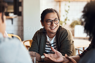 Buy stock photo Shot of a handsome young man sitting and smiling with his friends in a coffee shop during the day