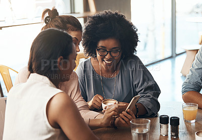 Buy stock photo Shot of attractive young women sitting together and smiling while looking at a cellphone in a coffee shop
