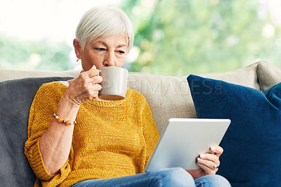 Buy stock photo Shot of a senior woman using a digital tablet and having coffee on the sofa at home