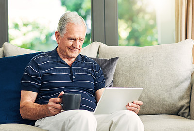Buy stock photo Shot of a senior man using a digital tablet and having coffee on the sofa at home