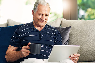 Buy stock photo Shot of a senior man using a digital tablet and having coffee on the sofa at home