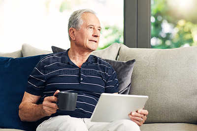 Buy stock photo Shot of a senior man using a digital tablet and having coffee on the sofa at home