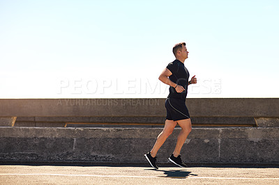 Buy stock photo Shot of a sporty young man out for a run on a bridge in the city