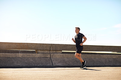 Buy stock photo Shot of a sporty young man out for a run on a bridge in the city