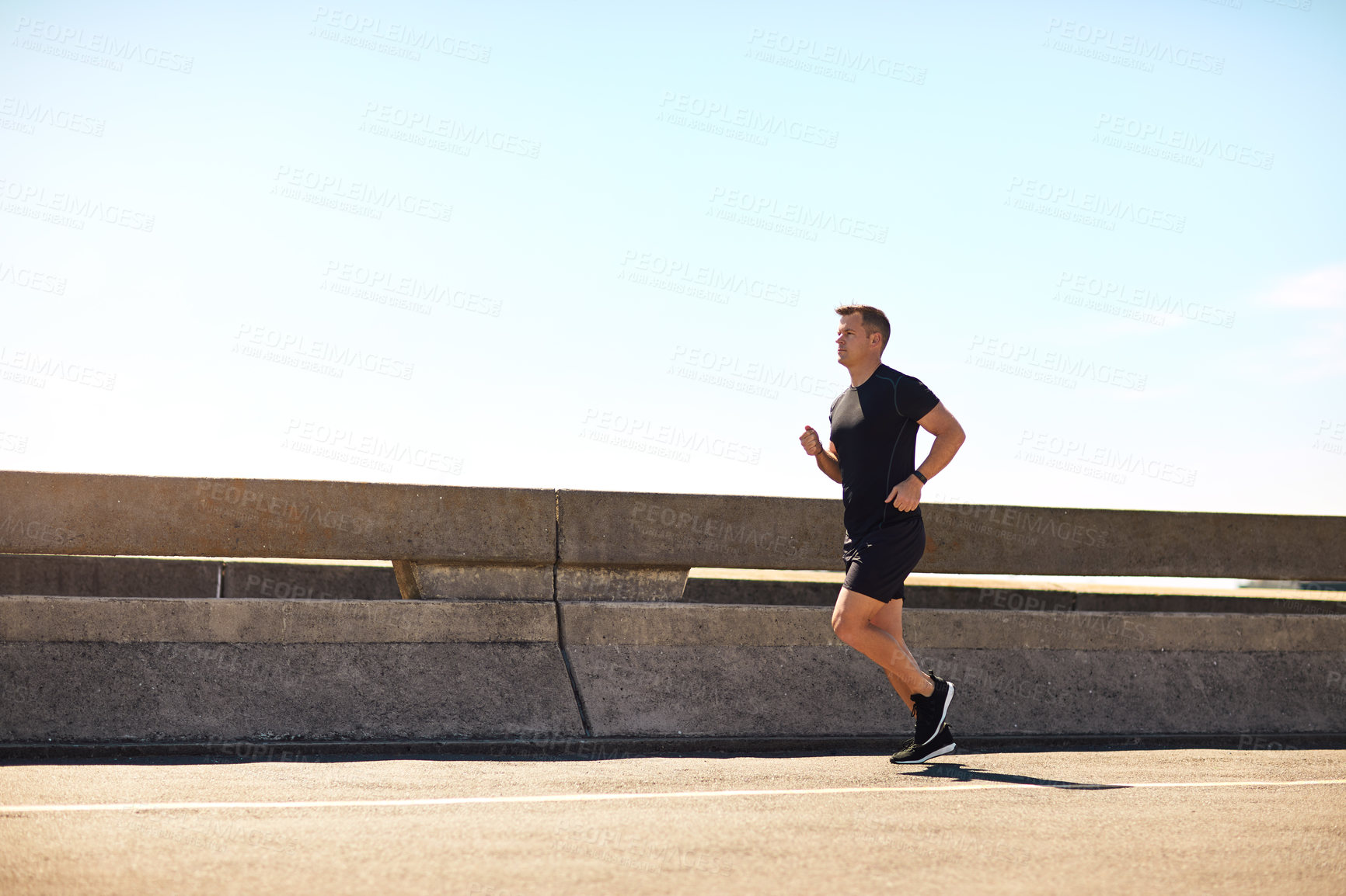 Buy stock photo Shot of a sporty young man out for a run on a bridge in the city
