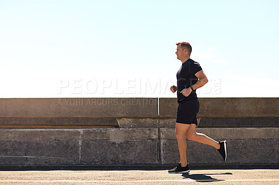 Buy stock photo Shot of a sporty young man out for a run on a bridge in the city