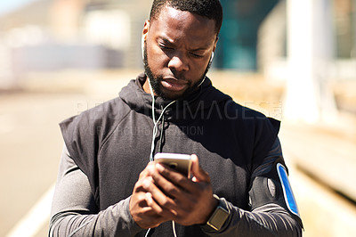 Buy stock photo Shot of a sporty young man using his cellphone while out for a run