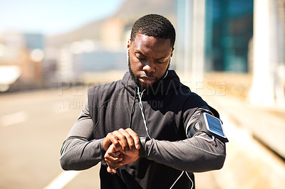 Buy stock photo Shot of a sporty young man looking at his wristwatch while out exercising