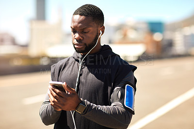 Buy stock photo Shot of a sporty young man using his cellphone while out for a run