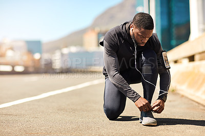 Buy stock photo Shot of a sporty young man tying his shoelaces while out for a run