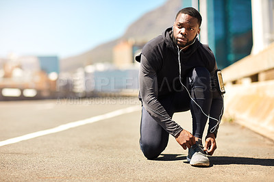 Buy stock photo Shot of a sporty young man tying his shoelaces while out for a run