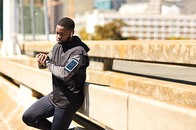 Buy stock photo Shot of a sporty young man looking at his wristwatch while out exercising