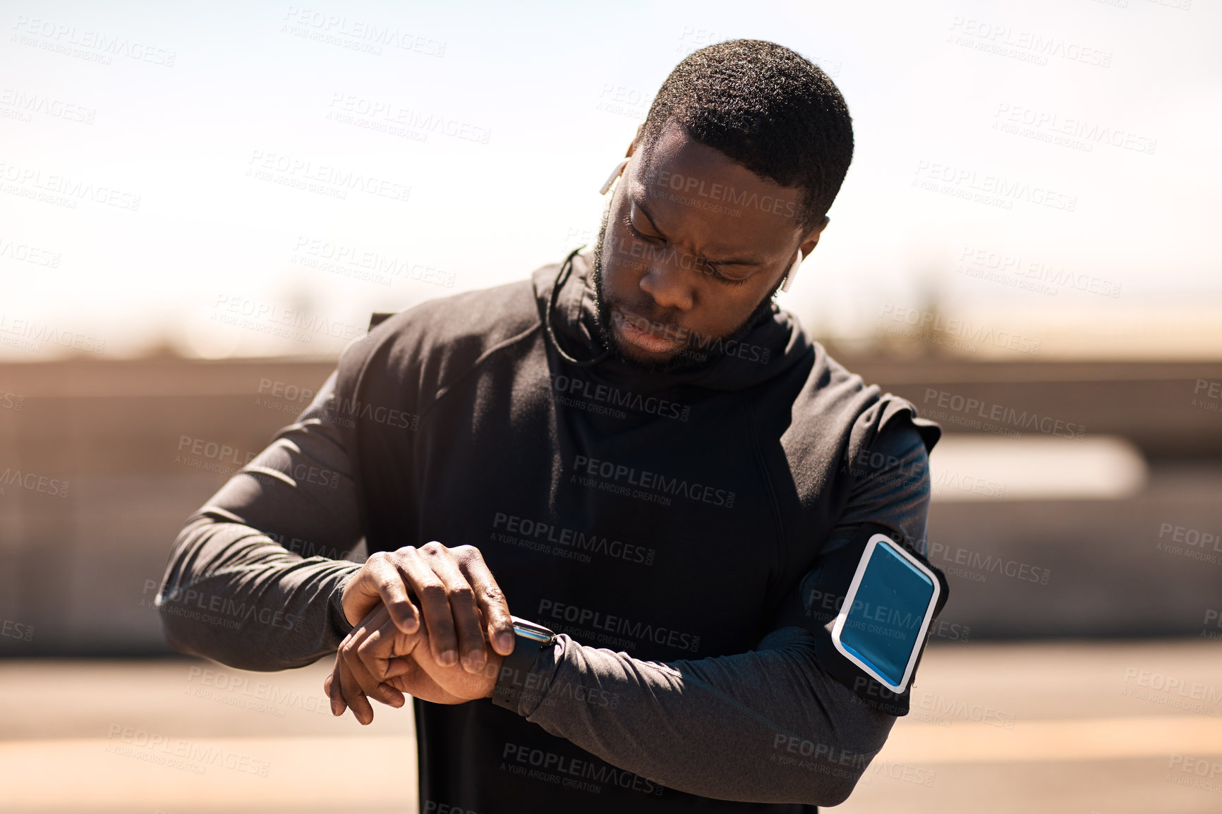 Buy stock photo Shot of a sporty young man looking at his wristwatch while out exercising