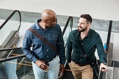 Buy stock photo Cropped shot of two businessmen talking while standing on an escalator in their office
