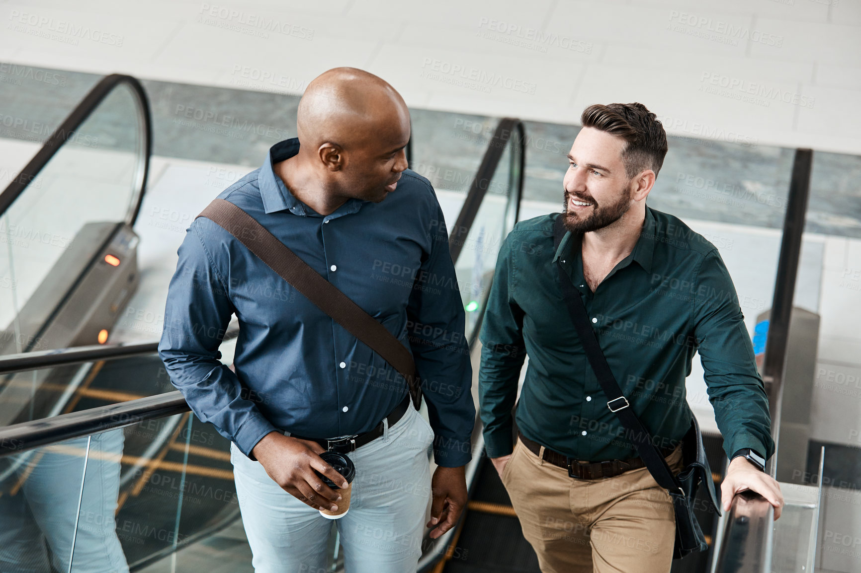 Buy stock photo Cropped shot of two businessmen talking while standing on an escalator in their office