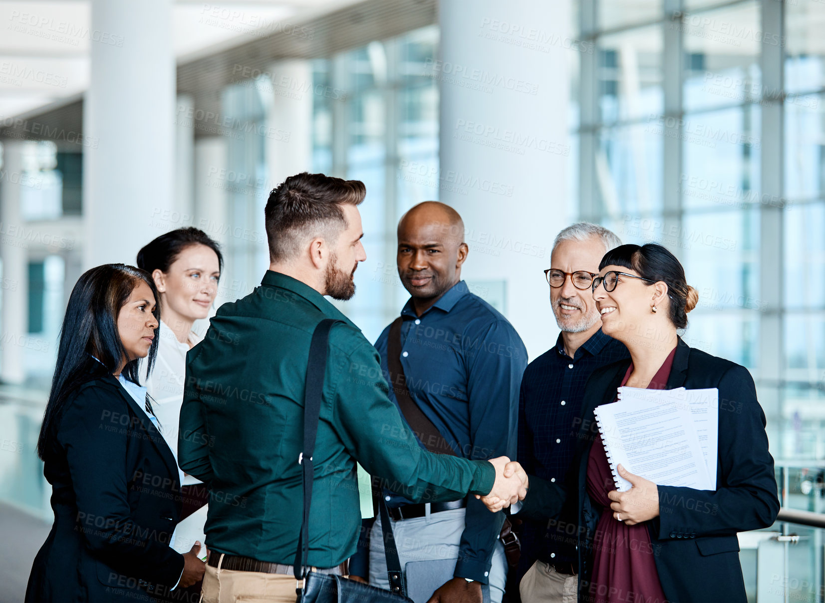 Buy stock photo Shot of two businesspeople shaking hands while their colleagues look on