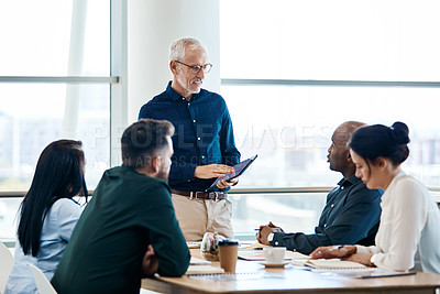 Buy stock photo Shot of a mature businessman using a digital tablet during a meeting with colleagues at work