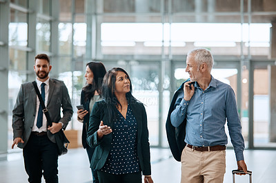 Buy stock photo Shot of a group of businesspeople conversing and walking with their luggage at an airpot