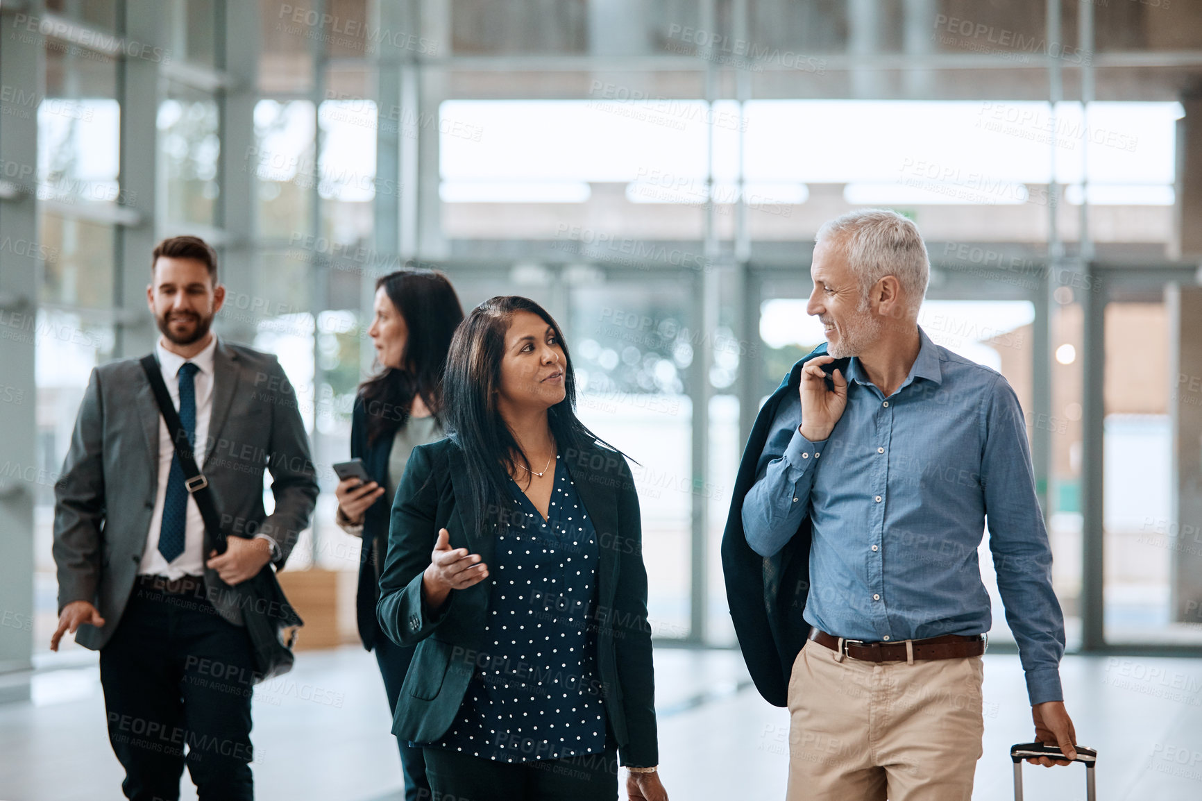 Buy stock photo Shot of a group of businesspeople conversing and walking with their luggage at an airpot
