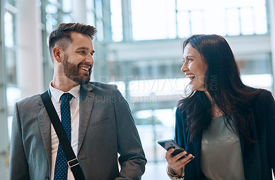Buy stock photo Shot of two cheerful young businesspeople walking and having a conversation together at work