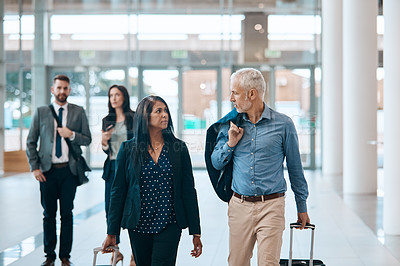 Buy stock photo Shot of a group of businesspeople conversing and walking with their luggage at an airpot