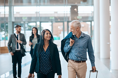 Buy stock photo Shot of a group of businesspeople conversing and walking with their luggage at an airpot