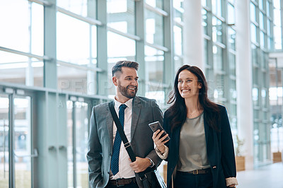 Buy stock photo Shot of two cheerful young businesspeople walking and having a conversation together at work
