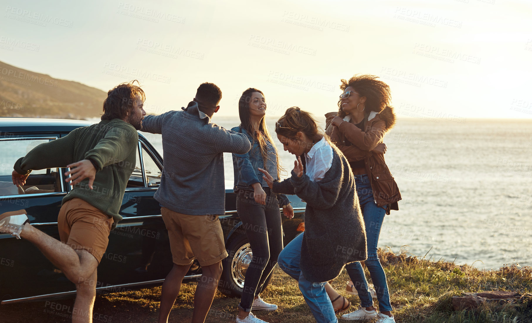 Buy stock photo Cropped shot of a diverse group of young friends standing together and dancing on the beach during a road trip