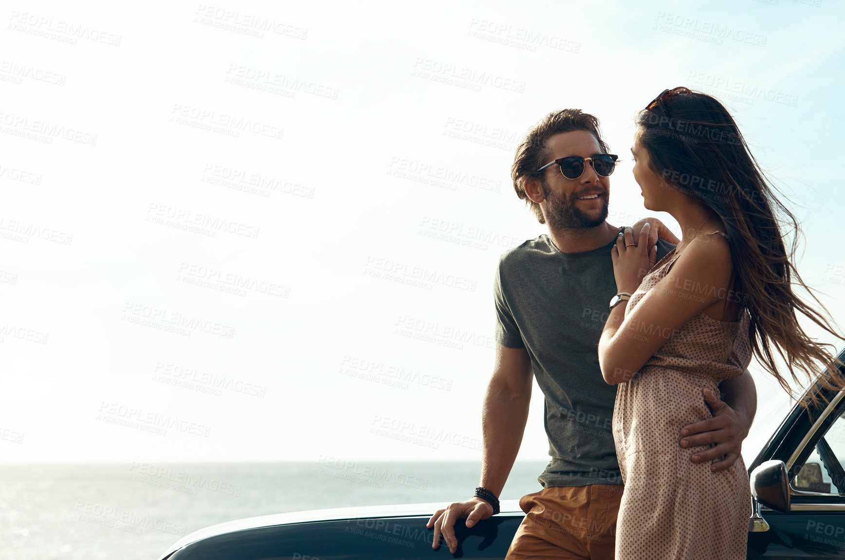 Buy stock photo Cropped shot of an affectionate young couple standing close to each other and leaning on a car by the ocean
